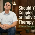 Therapist Douglas Carmody seated in a modern Tampa therapy office beside bold text reading “Should You Try Couples Therapy or Individual Therapy First?” with warm earth-tone décor and calming editorial-style lighting.